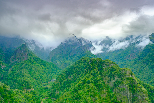 Panoramic view over the beautiful green mountains from levada Balcoes, Madeira, Portugal with clouds touching the mountains during an overcast summer day.