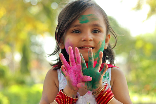 Happy small girl of Indian ethnicity playing Holi with colored powder outdoors in the nature.