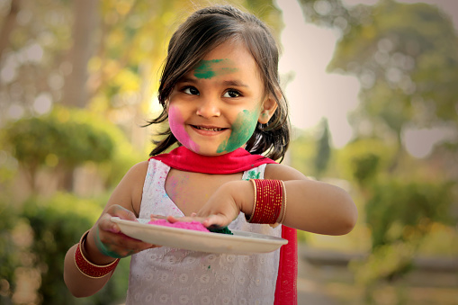 Small girl of Indian ethnicity celebrating Holi festival outdoors in the nature.