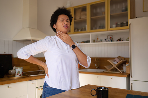 Displeased African American woman feeling discomfort in her throat at home.