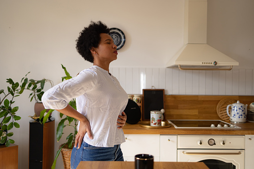 Displeased African American woman holding her stomach in pain in the kitchen.