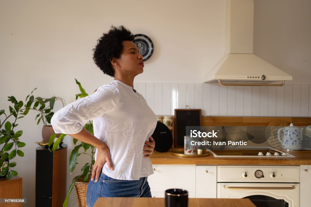 Mid adult black woman having stomachache at home. Displeased African American woman holding her stomach in pain in the kitchen. Gastroesophageal Reflux Disease Stock Photo