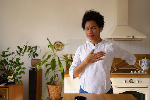 Worried African American woman feeling pain in her chest in the kitchen. Copy space.