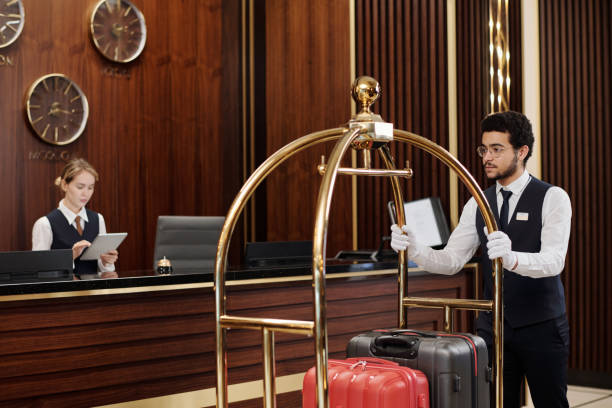 istock Young bellboy in uniform pushing cart with suitcases along reception counter 1471856560
