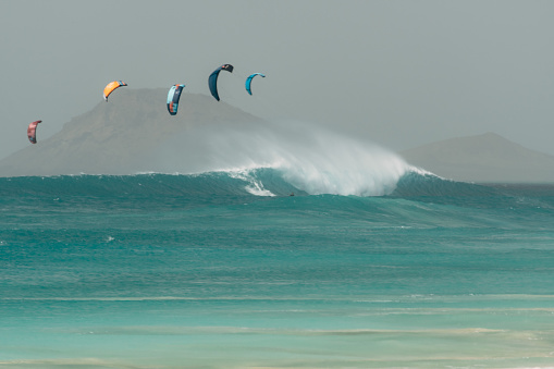 Panoramic view of a very big wave in the Atlantic with 5 kite sails in front of the silhouette of the island of Sal (Cape Verde Islands)