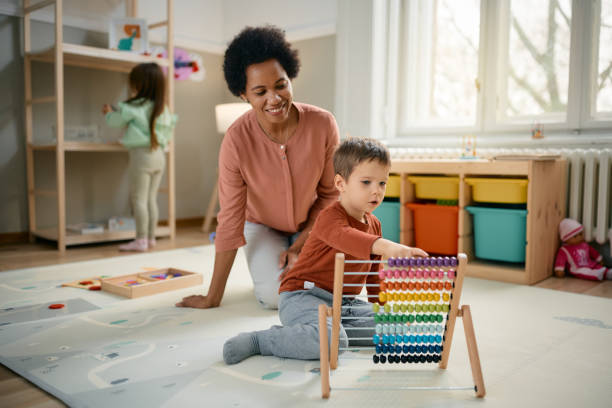 istock Little boy using abacus while learning to count with teacher's assistance at kindergarten. 1471858392