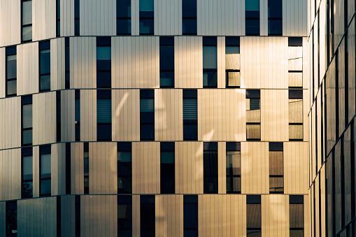 The golden evening sun is reflected in a metal facade of a modern architecture with many windows
