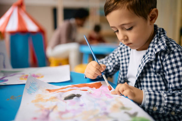 istock Small boy using watercolors while drawing on the paper at kindergarten. 1471858534
