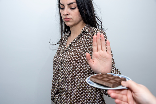 Young girl on a diet and doesn't want to eat sweets.With her raised hand, she refuses to take a white plate of sweets offered by her friend. A healthy way of life.