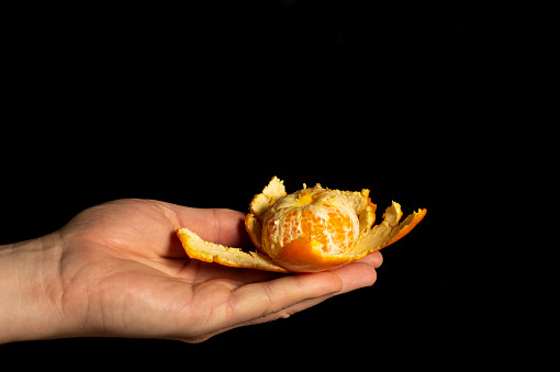 Hand holding ripe tangerine with peel on black isolated background