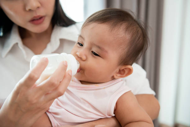 A baby girl is drinking milk bottle in mother arms, family, child, childhood and parenthood concept stock photo