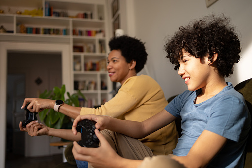 Happy African American boy having fun while playing video games with his single mother in the living room.