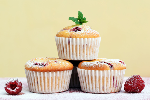 Muffins with raspberries on sugared background with fresh fruits, decorated with melissa leaves