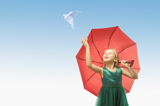 girl in a green dress and a dove flying from her hand on blue sky background. concept of peace, no war.