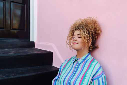 Relaxing on the doorstep: Young woman with Afro hair finds serenity at home.