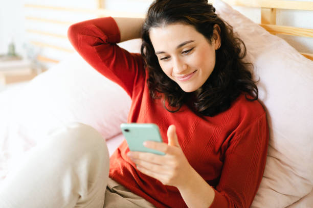 Beautiful young woman using her smartphone on the bed - fotografia de stock