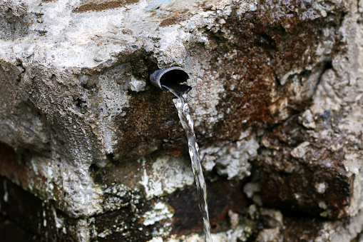 water flowing from a pipe with a natural stone background in an outdoor fountain