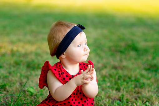 portrait of a cute baby in summer on the green grass in a red bodysuit in the setting sun