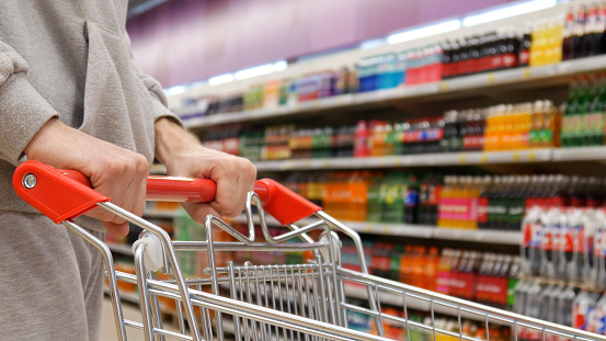 A shopping trolley in the drinks department close-up and a buyer's hands rolls it