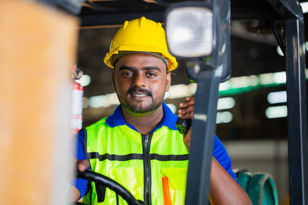 istock Worker man in hardhat and safety vest driving forklift for control loading box, Warehouse forklift loader works with goods 1471881949