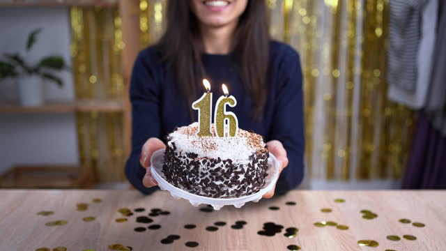 Holidays and celebration concept. Excited woman celebrating 16 birthday, blowing candle number sixteen on cake, wearing party cake and having fun on camera. Point of view or POV.