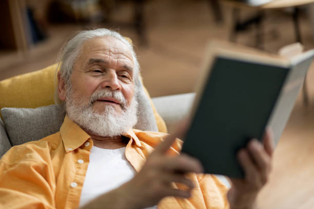 istock Positive elderly man laying on couch, reading book 1471882961