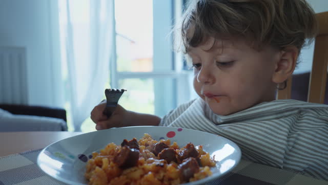 Child eating hot food burning mouth. One small boy spitting pasta out on plate. Kid eats lunch