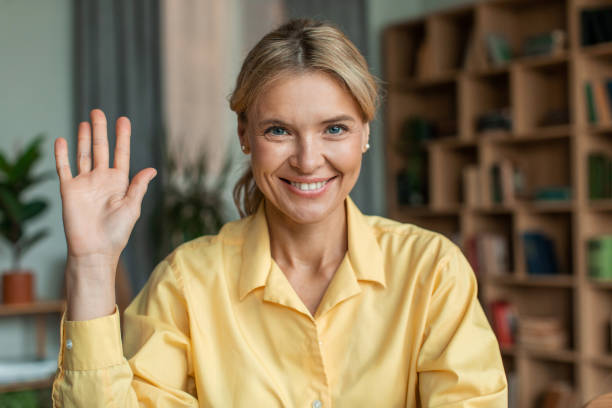 blogueuse d’affaires heureuse dans des écouteurs sans fil donnant un webinaire ou enseignant en ligne, saluant la main à la caméra, souriant - working smiling equipment car photos et images de collection