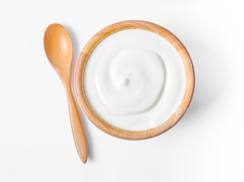 Fresh greek yogurt in wooden bowl with wooden spoon on white background. Healthy breakfast.