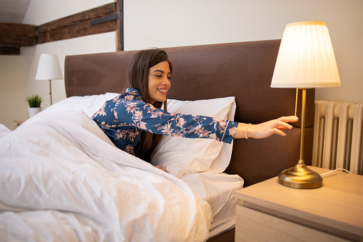 Happy young woman turns off the lamp and goes to sleep after a long day.
