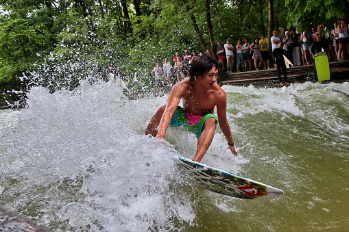 Munich, Germany - Jun 04, 2022: Surfer in the city river, Munich is famous for people surfing in urban enviroment called Eisbach