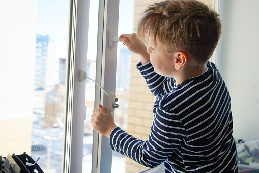 safety at home for small children. a lock on the window protects children from opening the window. The boy tries to open the window standing on the windowsill on a high floor.