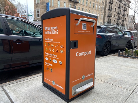 New orange NYC Department of Sanitation Smart Compost Bin for composting food scraps that opens with a smartphone on a sidewalk in Manhattan, New York City, USA