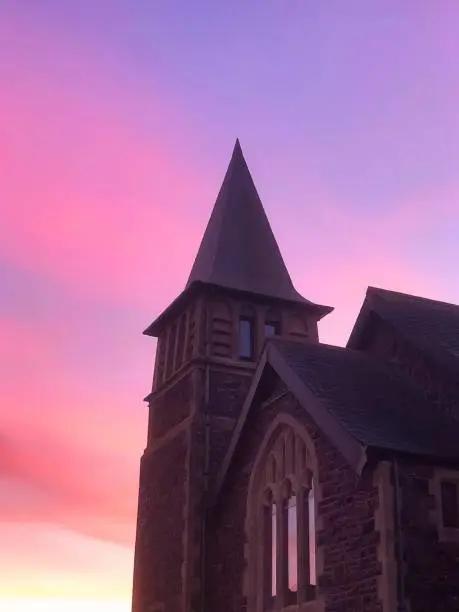 Old Church building against a vibrant red, pink and yellow sky and sunset with old religious architecture and windows, a catholic style building with old stone and design
