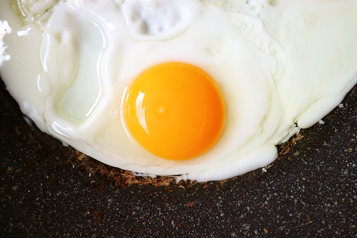 Closeup of a vibrant color hen egg being fried in a pan