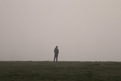 Man standing on hill in the mist and fog, a mysterious figure with fog creating a dreamy, atmospheric, mysterious scene on an outdoor field with dewy mist around a man standing alone on a hill