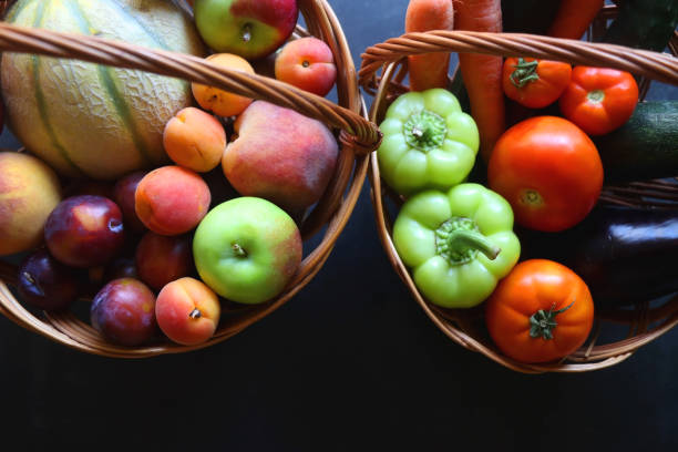Two wickers baskets with healthy seasonal fruit nad vegetable. Dark background, top view.
