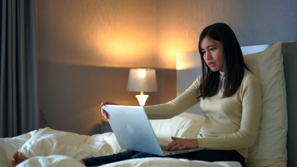 Young woman sitting on bed using laptop for work in bedroom at home. stock photo