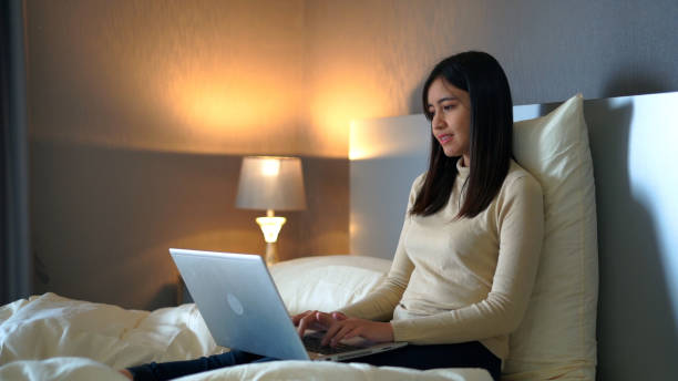 Young woman sitting on bed using laptop for work in bedroom at home. stock photo