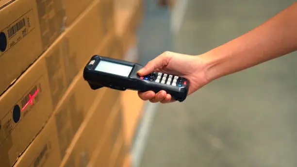 Photo of Close up hand scanning products with barcode scanner in warehouse.