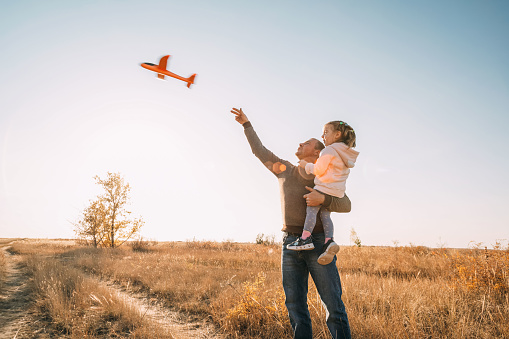 Happy Father And Child Having Fun Playing Outdoors. Smiling Young Dad And Daughter Spending Time Together, let an airplane into the sky