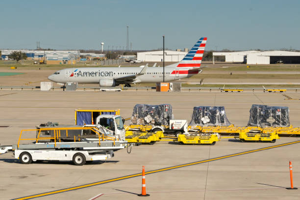 Airport ground handling equipment with an American Airlines passenger jet in the background Austin, Texas - February 2023: Luggage loading equipment and air freight pallets on the tarmac at the city's airport. An American Airlines Boeing 737 jet is taxiing for take off in the background. austin airport stock pictures, royalty-free photos & images