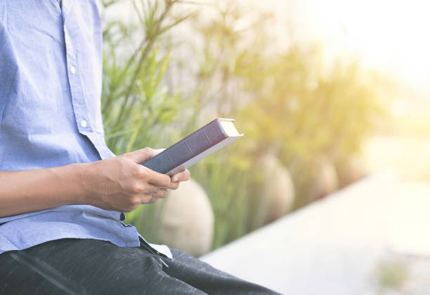 istock Closeup man holding book or bible with sunlight and nature background. 1471906434