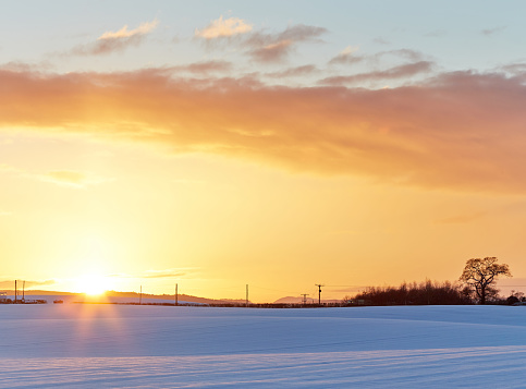 Beautiful yellow and orange sunset sky over a snowy field.