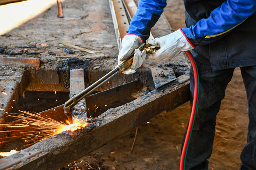 Man using torch to cut metal, using industrial safety, lather gloves.