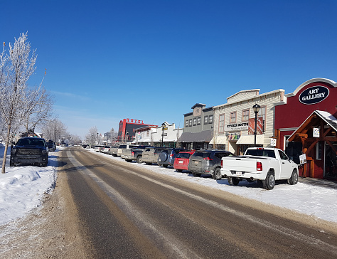 Cochrane, Alberta, Canada - March 1,2023 : Small town Alberta. Main Street. Small independent business. Frost on the trees.  Dirty Cars Parked.  Hotel in background.