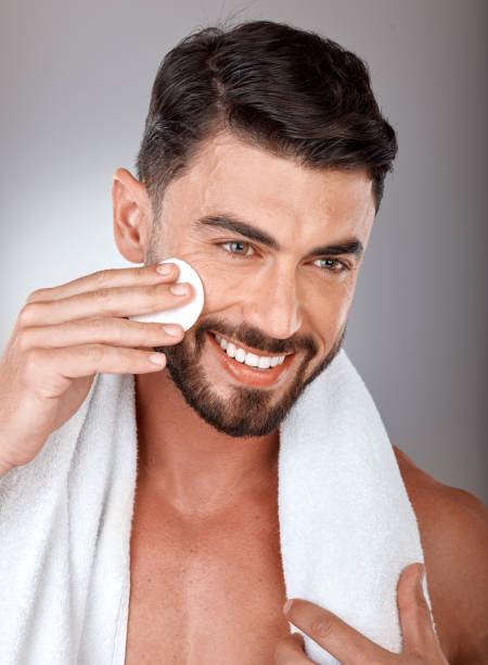 cosméticos, cuidado de la piel y hombre con algodón, belleza natural y sobre fondo de estudio gris. hombre, chico y maquillaje con algodón, tratamiento y rutina con sonrisa, toalla y saludable para lujo y spa - male towel men human face fotografías e imágenes de stock