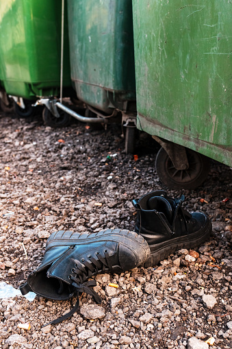 Worn-out black shoes by garbage containers on the street, selective focus