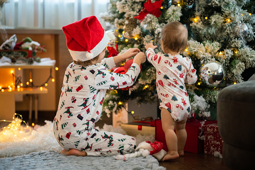 Rear view of boy and baby girl decorating Christmas tree while wearing pajamas at home