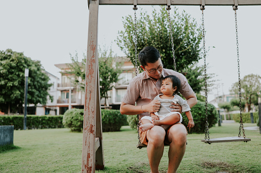 Asian man sitting on the swing set with his lovely babygirl, enjoy his life with his beloved.